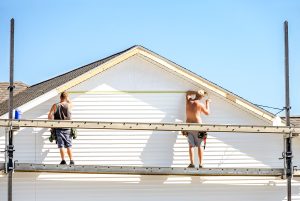 Two workers on scaffolding installing siding on a house